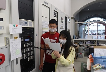 館内放送をする日本人学生（左）と留学生（右）【関C】